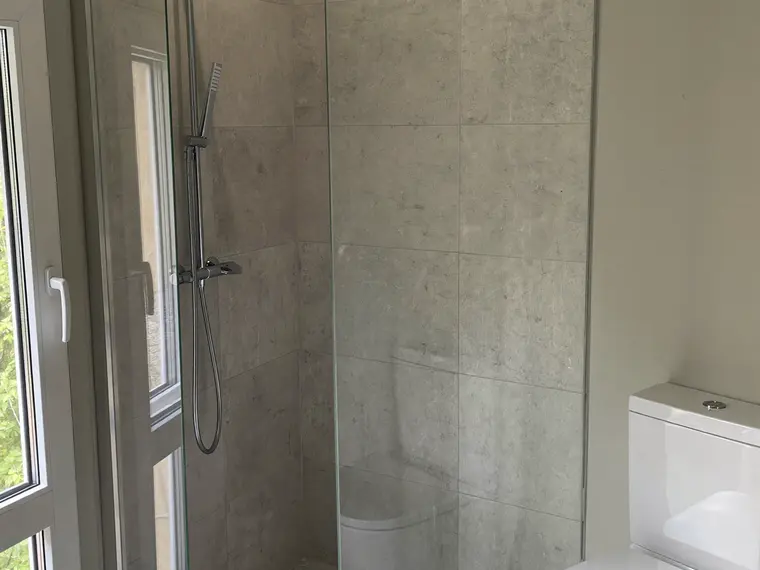 Fertiges kleines Bad mit bodengleicher Dusche, Glaswand, Linienentwässerung und wandhängendem WC in hellgrauen Fliesen.