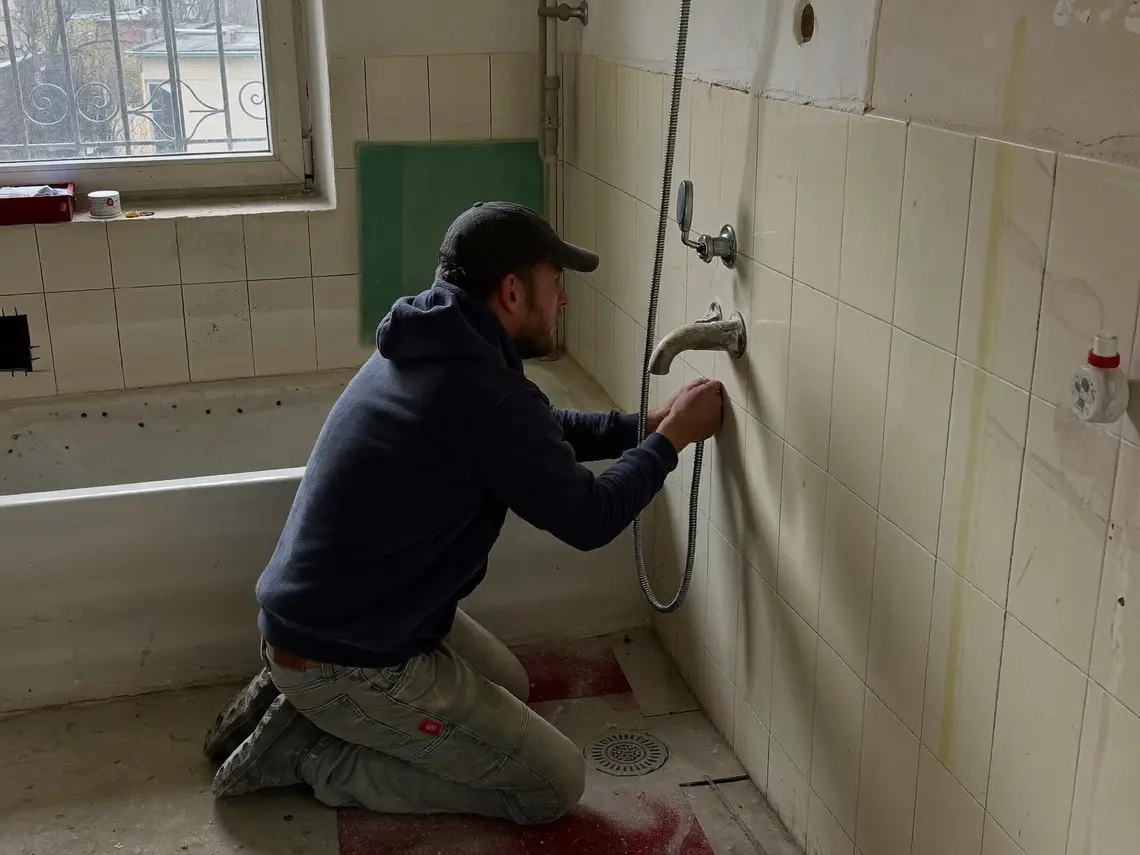 Bad im Umbau: ein Installateur kniet auf einer Schutzmatte und setzt einen Duschablauf in den Estrich, wo zuvor die Badewanne stand.