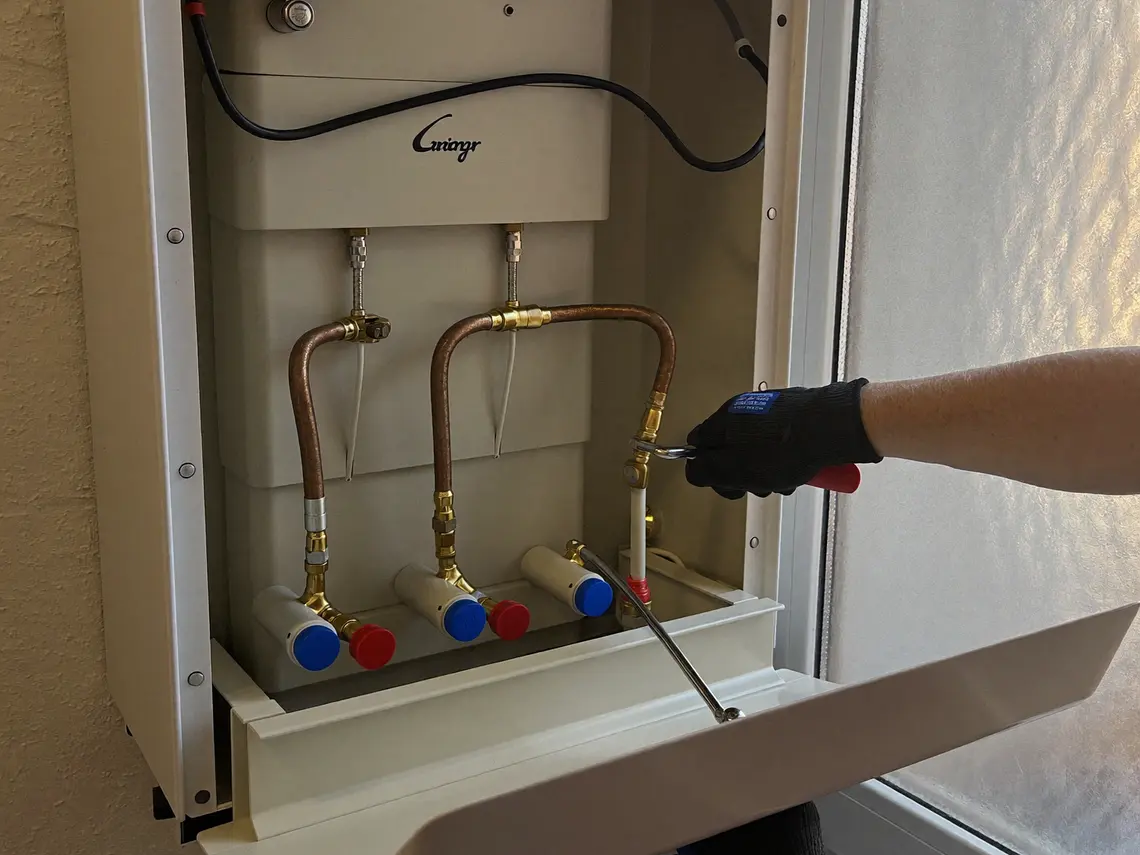 Neu montierter wandhängender Gasbrennwertkessel mit geöffneter Verkleidung, sauber verlegten Kupferanschlüssen und einem Verteiler mit roten und blauen Kappen.